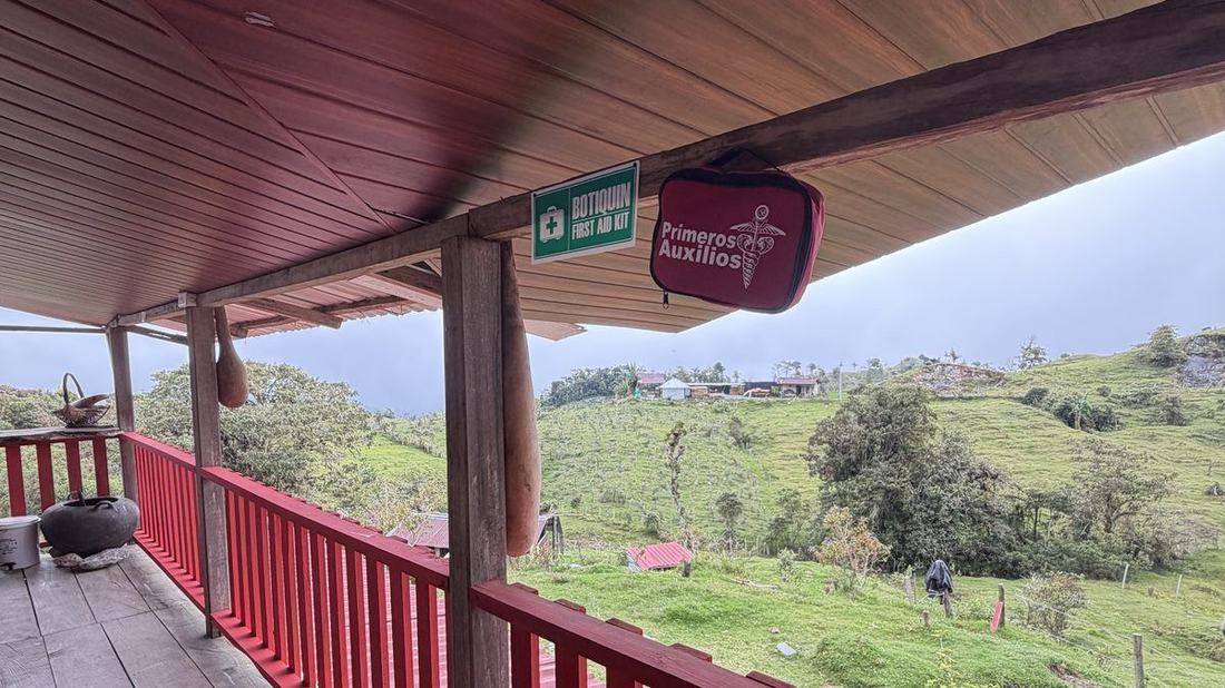 Corredor exterior de madera con baranda roja, techo entablado y vista panorámica al valle verde de El Peñón