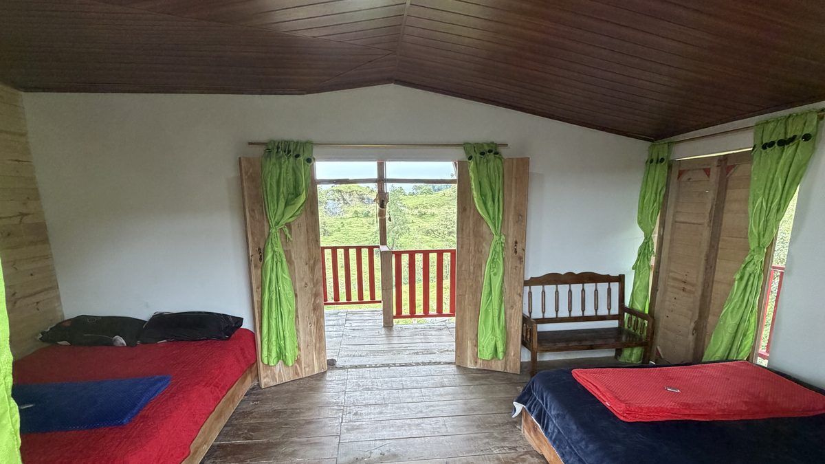 Interior amplio de habitación con techo de madera a dos aguas, dos camas y puertas abiertas al corredor con vista a la montaña